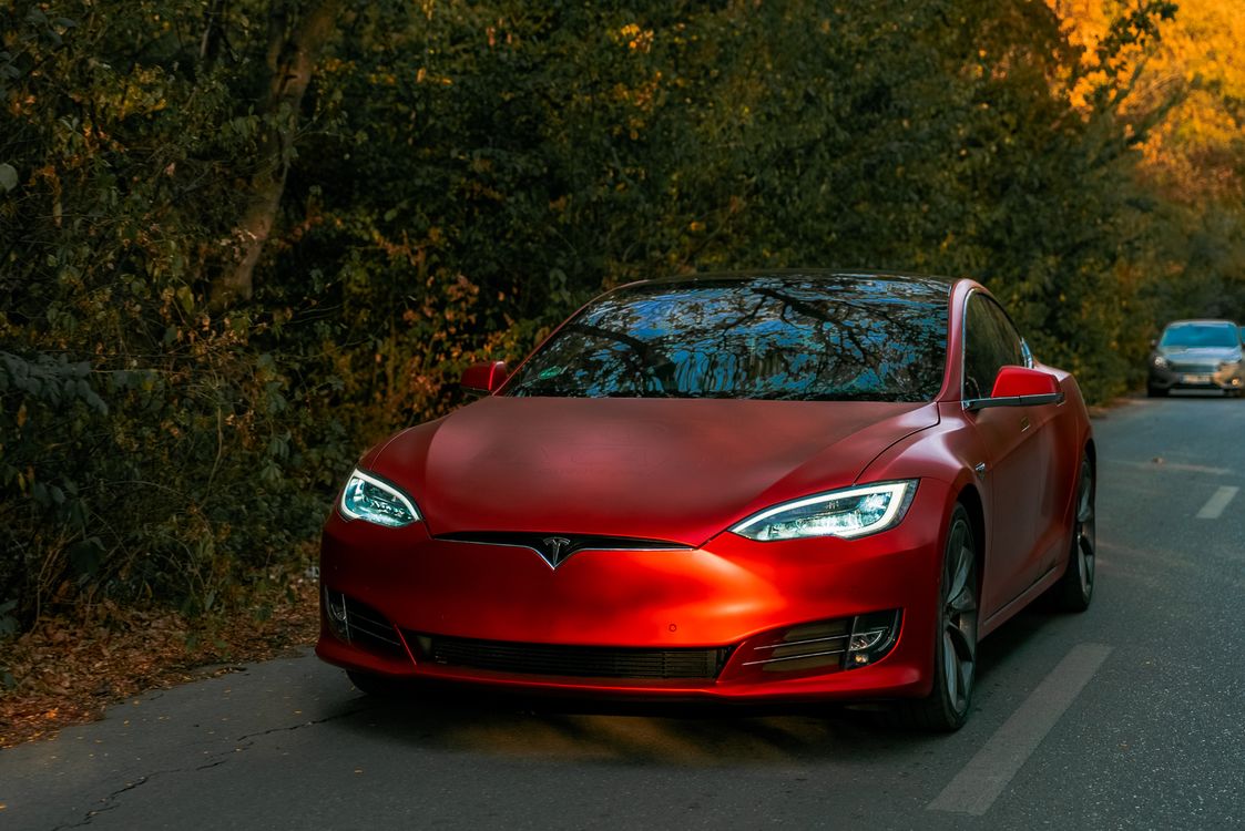 Red Tesla Model S driving on a forest road in autumn